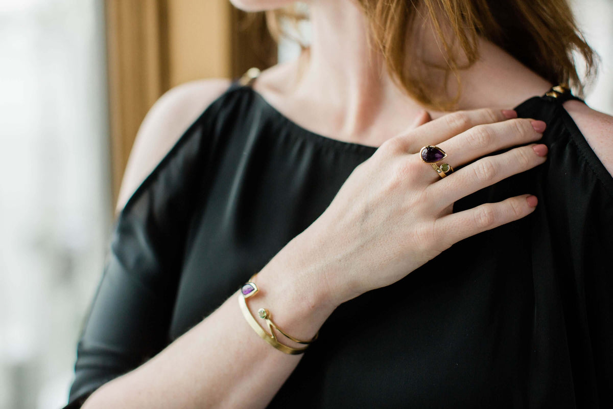 A model wears an 18k gold ring with amethyst and peridot, a gap ring