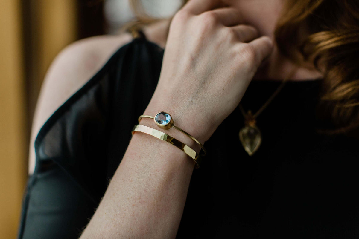 A model wears a 18k gold cuff bracelet with swiss blue topaz