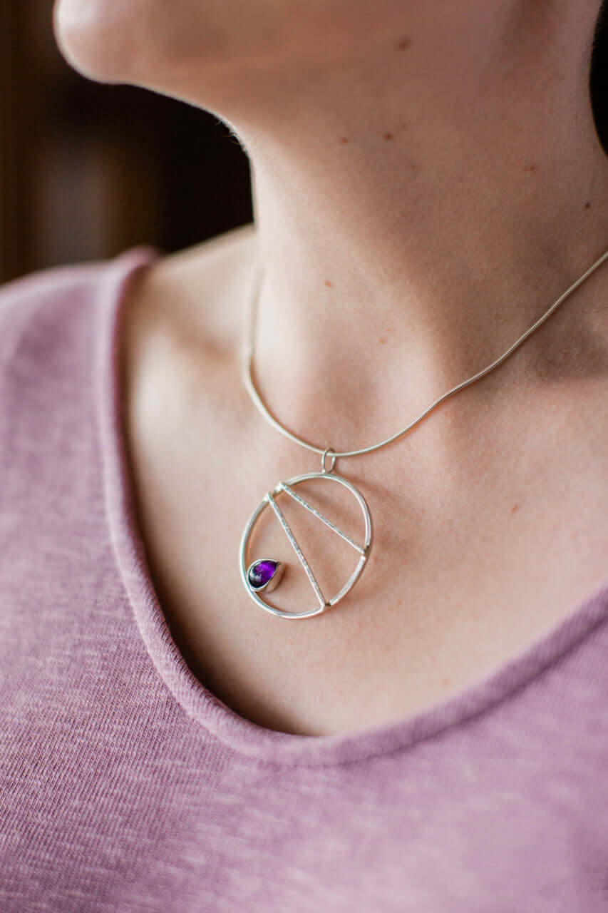 A woman wears a purple shirt and a handmade sterling silver crossbar necklace with amethyst