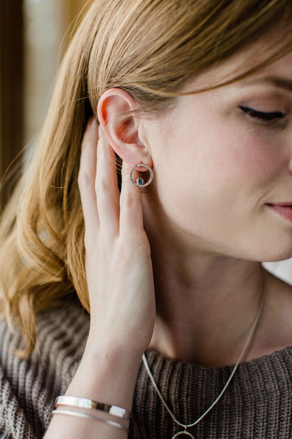 A model wears a pair of sterling silver circle studs with Swiss blue topaz