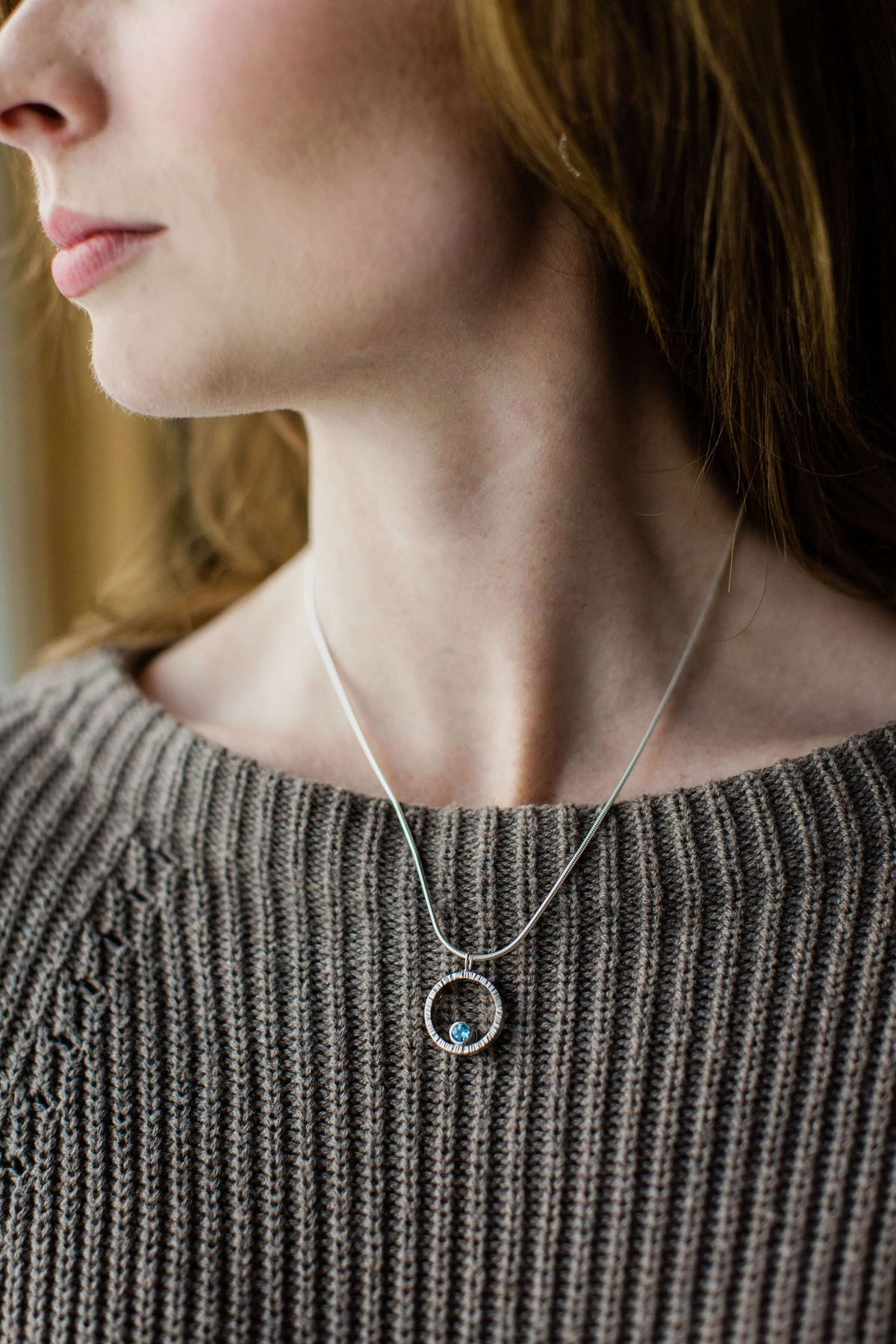 A hammered circle pendant necklace with Swiss blue topaz worn by a necklace
