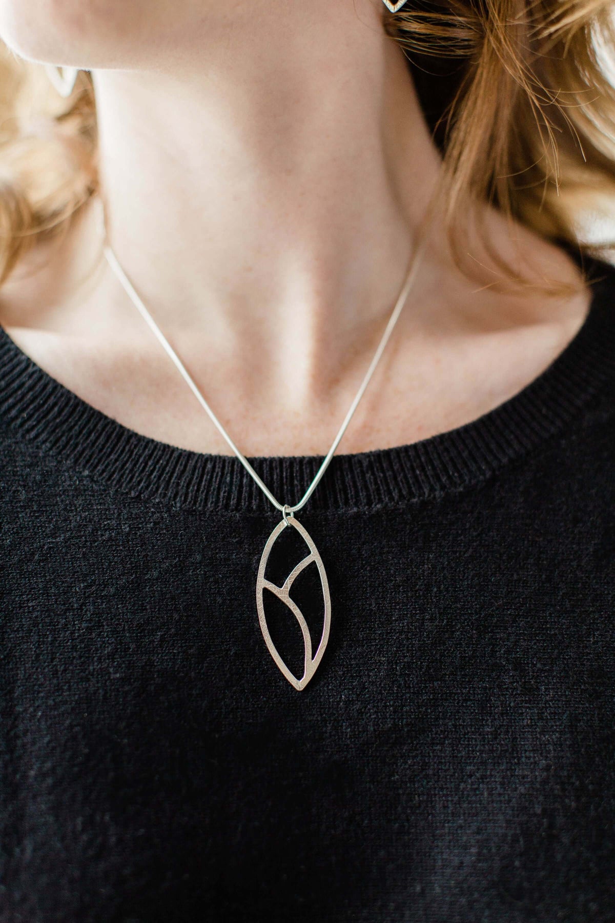 a handmade silver leaf necklace is shown worn around a woman&#39;s neck on a silver chain