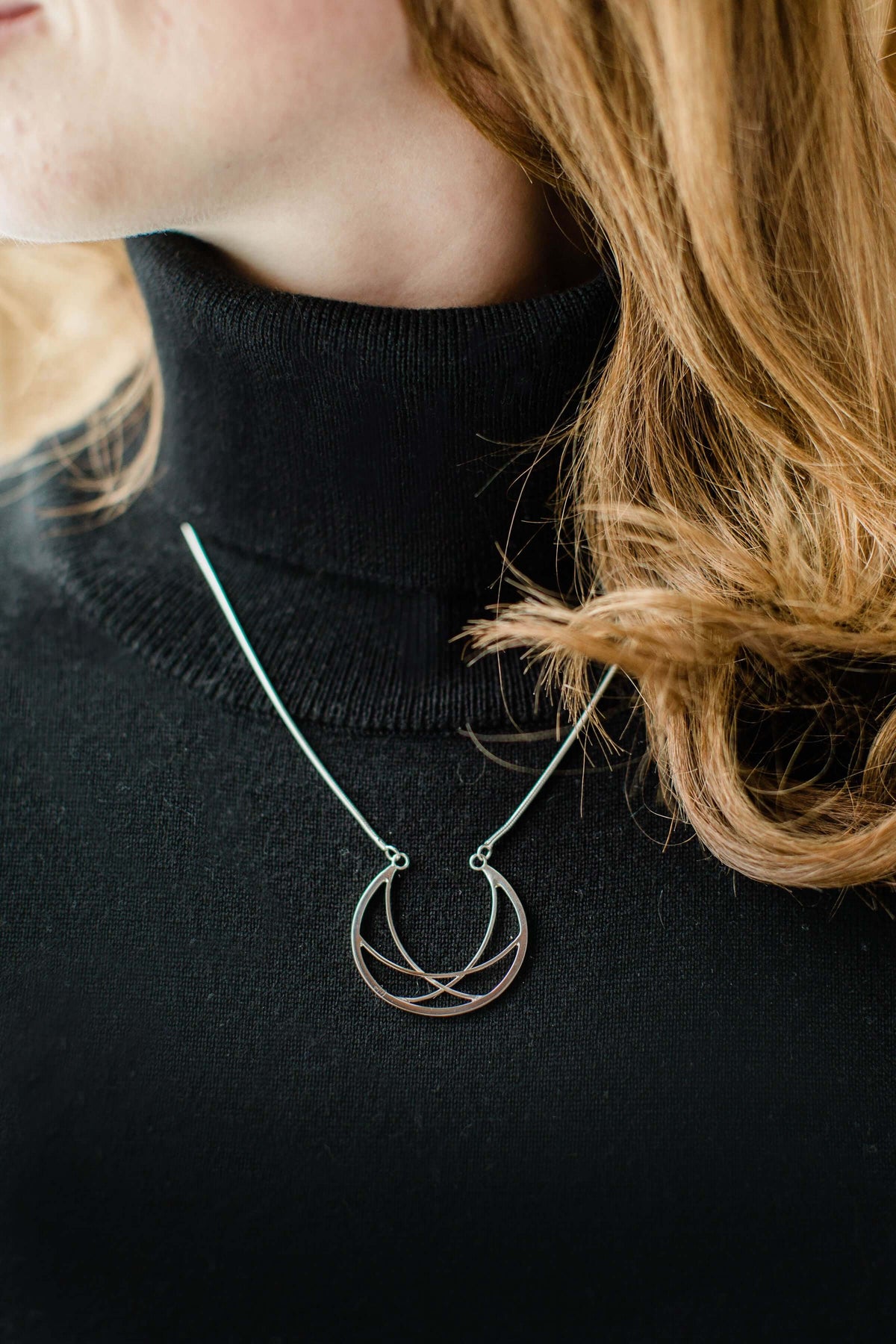 A woman wears a black sweater with handmade sterling silver crescent necklace