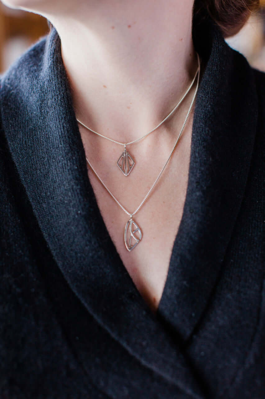 A woman wears a black sweater and woven silver necklace layered with a silver art deco necklace
