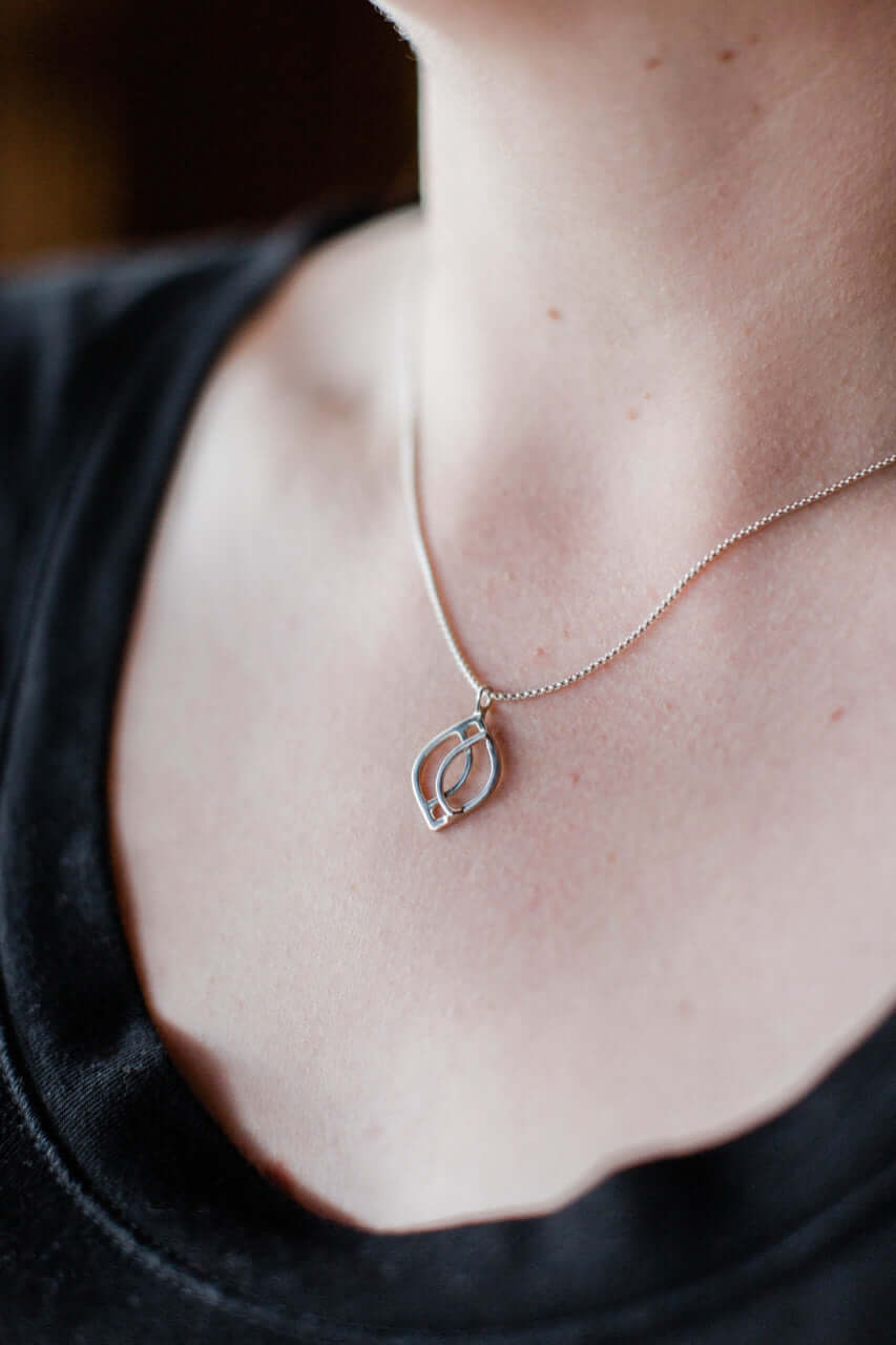 A sterling silver wave pendant is worn around a woman&#39;s neck on a silver chain