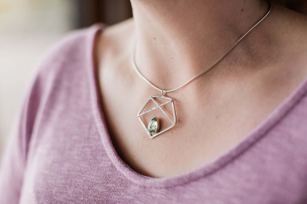A woman wears a purple shirt with a handmade sterling silver pentagon necklace with green prasiolite
