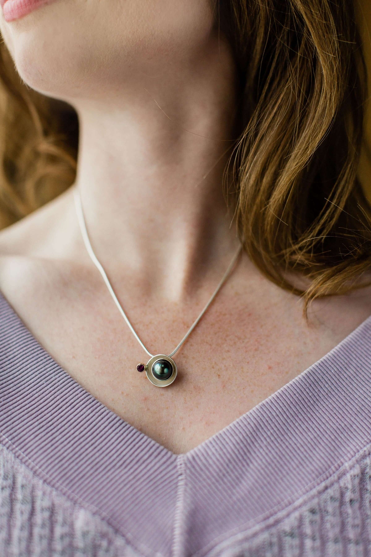 a model wears a tahitian pearl planet pendant with garnet stone