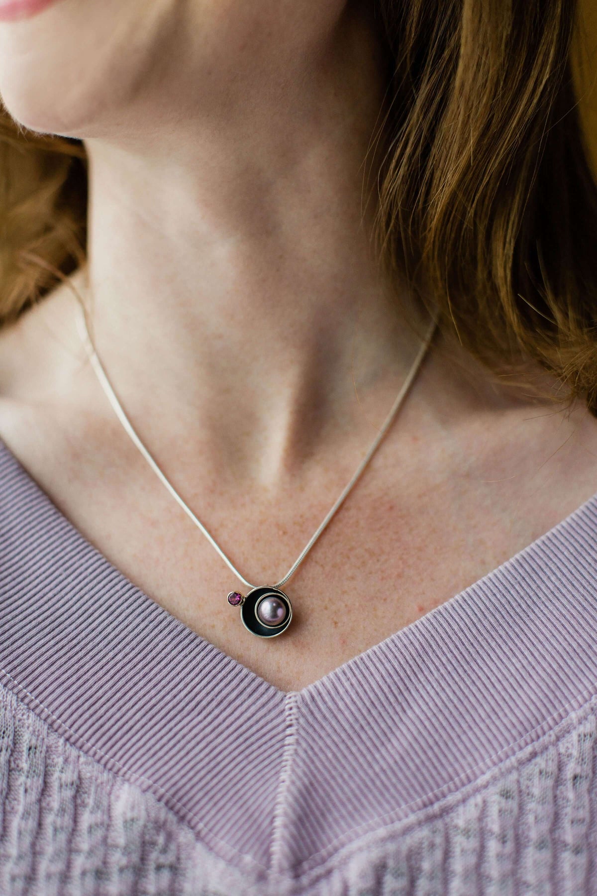 A woman wears a purple sweater and handmade sterling silver and pearl planet pendant