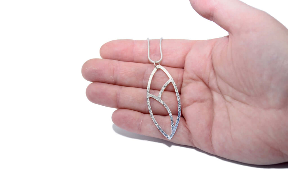 a large silver leaf necklace is shown on an adult&#39;s hand