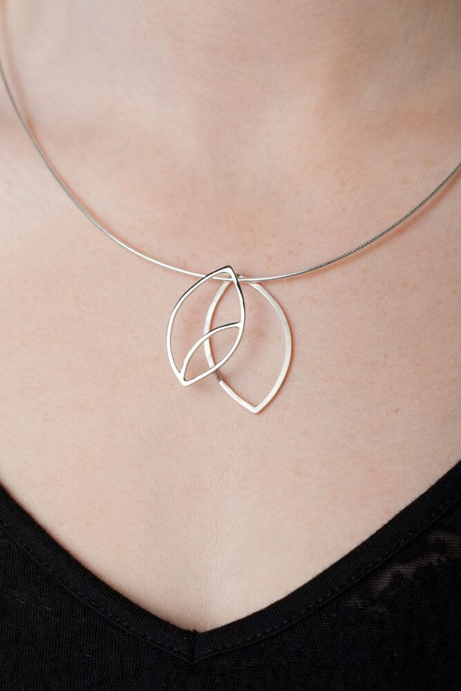 A sterling silver leaf pendant worn on a silver chain around a woman&#39;s neck