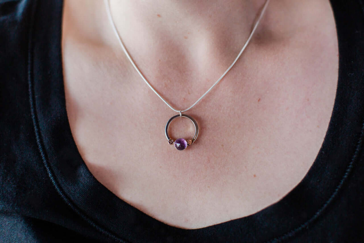 A woman wears a black shirt and silver chain with amethyst and rose gold pebble