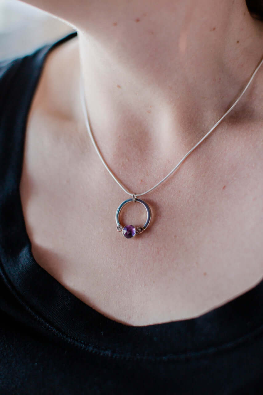 A woman in a black shirt wears a handmade sterling silver necklace with amethyst and rose gold pebble.