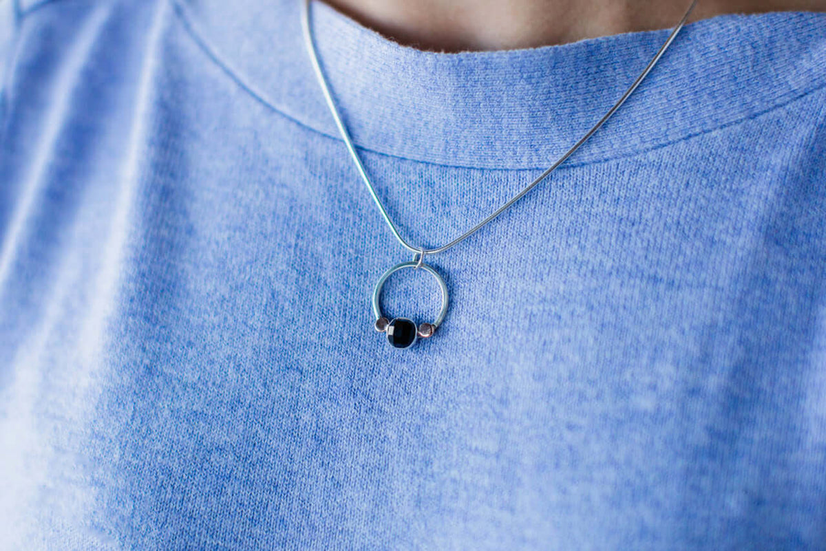 A woman wears a light blue shirt with handmade sterling silver black onyx pendant