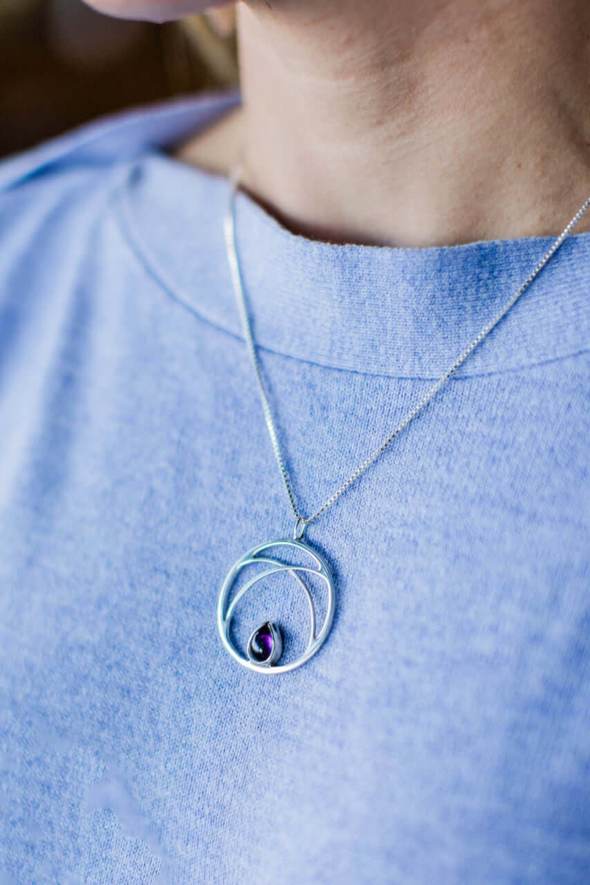 A woman in a blue shirt wears a necklace with circle pendant on a silver chain