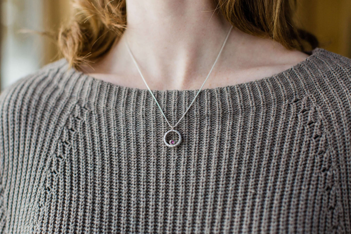 A model wears A sterling silver hammered circle pendant with garnet