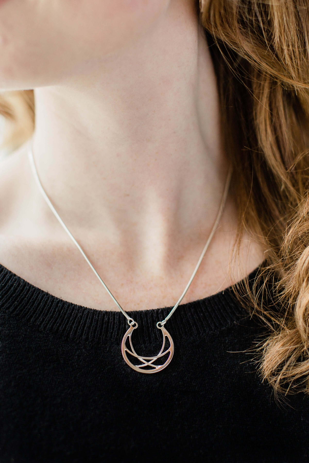 A woman wears a black sweater and handmade sterling silver sterling silver crescent necklace
