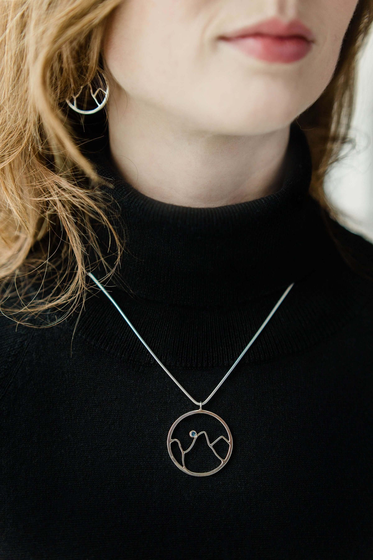 A woman wears a handmade sterling silver mountain pendant necklace with matching earrings