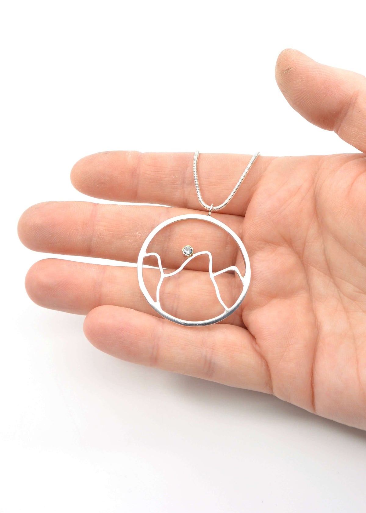 a woman holds a handmade sterling silver mountain pendant necklace with sky blue topaz